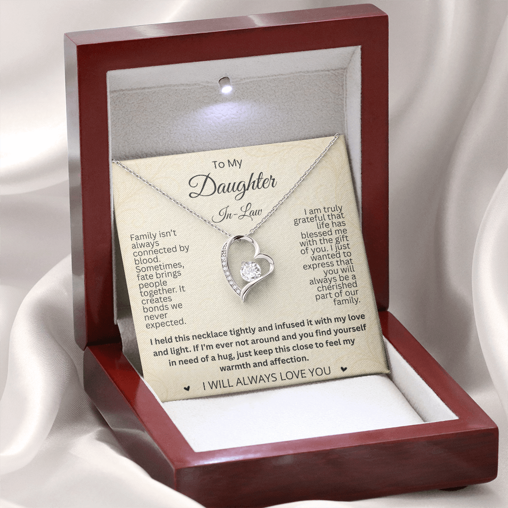 Silver-tone heart necklace and daughter-in-law card displayed upright in an illuminated reddish-brown gift box on white fabric.