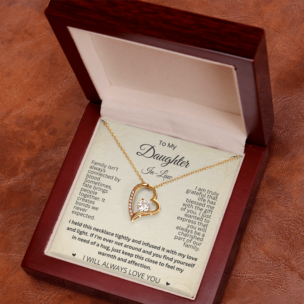 Angled view of a gold-tone heart necklace and daughter-in-law card in a reddish-brown gift box on a brown textured surface.