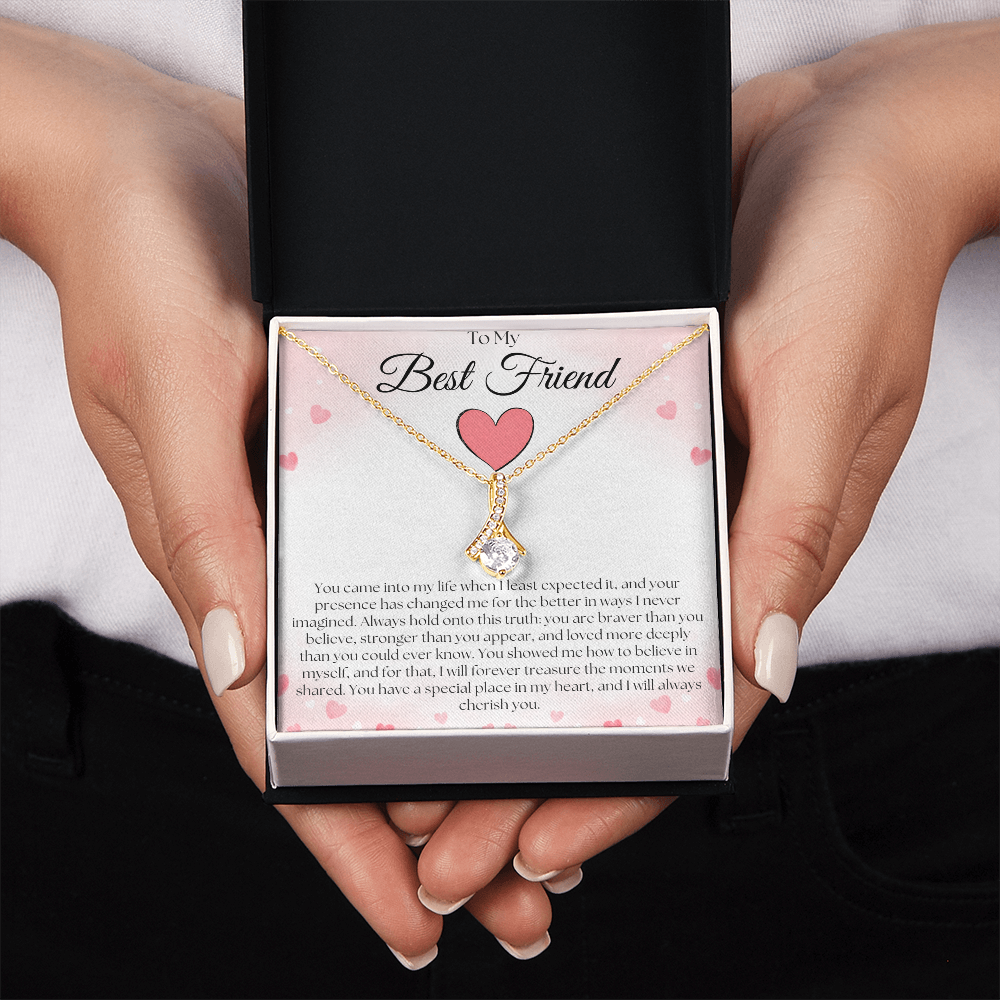 Hands holding a black and white gift box with a gold-tone pendant necklace and pink-heart best-friend card.