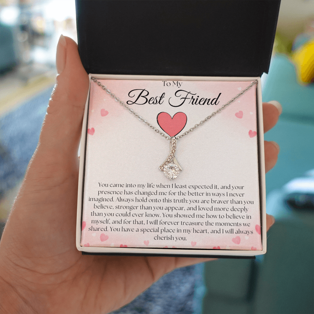 Hand holding a black and white gift box with a silver-tone pendant necklace and pink-heart best-friend card indoors.