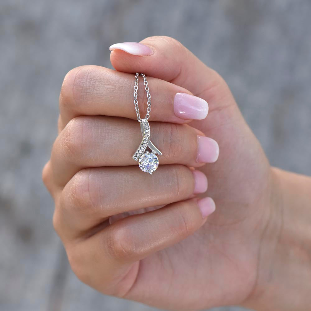  Close-up of a hand holding the white gold-finish ribbon pendant with a round cubic zirconia stone.