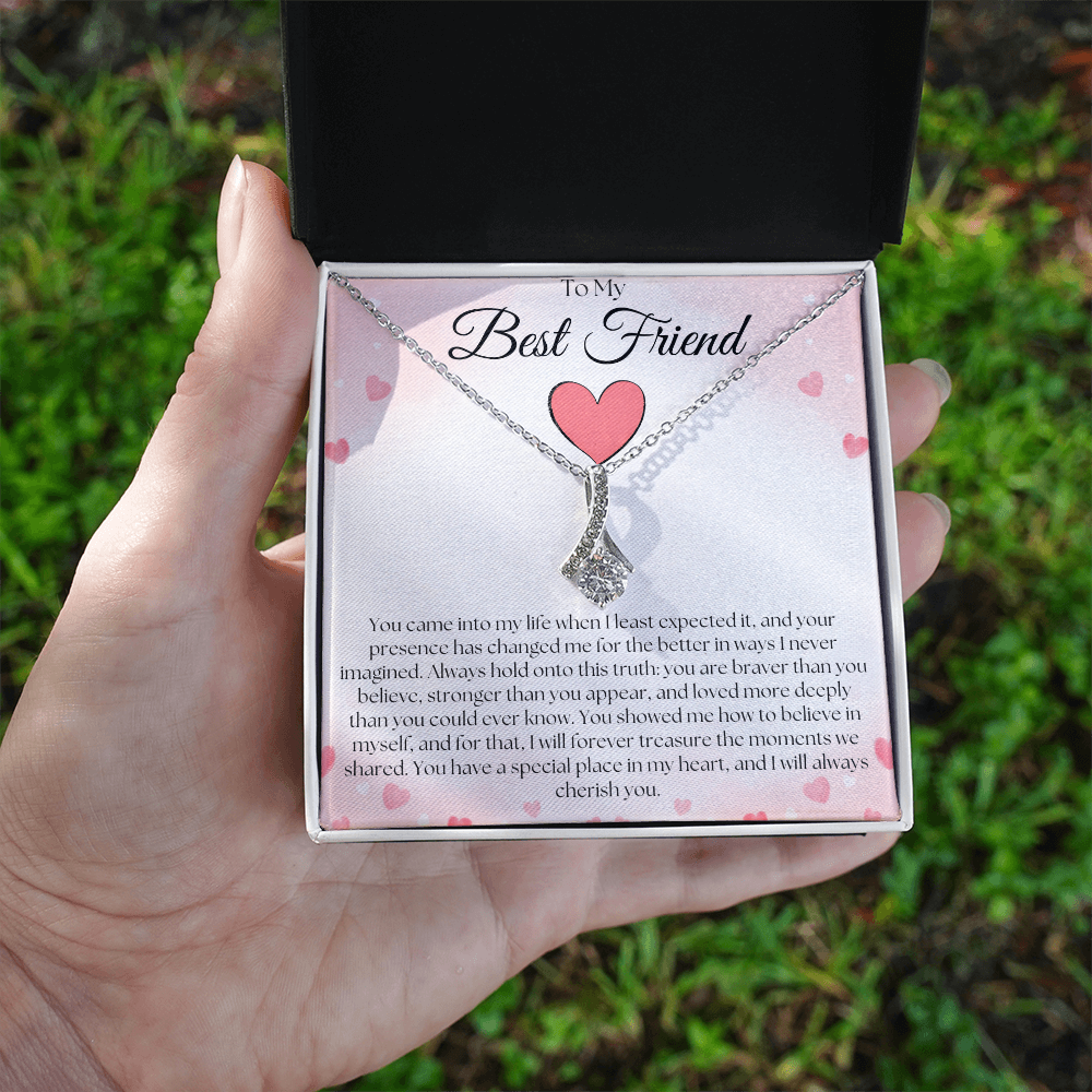 Hand holding a black and white gift box with a silver-tone pendant necklace and pink-heart best-friend card outdoors.