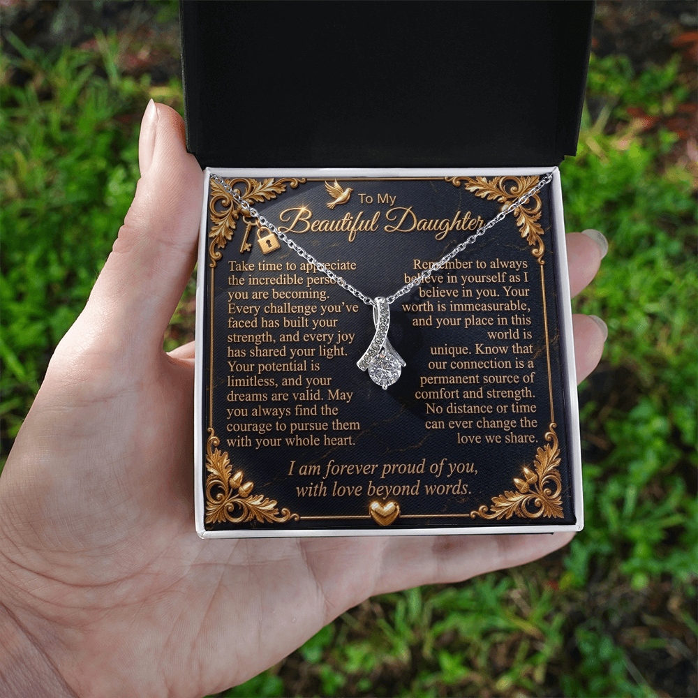  Hand holding an open standard gift box with a white gold-finish necklace and daughter message card outdoors.