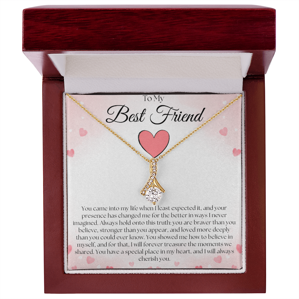 Gold-tone pendant necklace and pink-heart best-friend card in an open reddish-brown gift box on white.