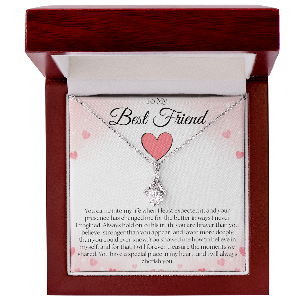 Silver-tone pendant necklace and pink-heart best-friend card in an open reddish-brown gift box on white.