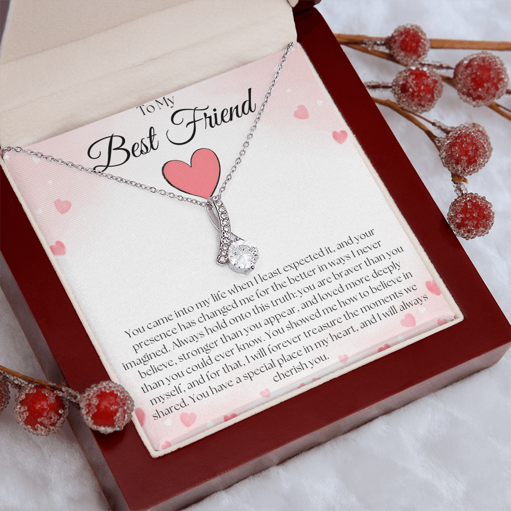 Silver-tone pendant necklace and pink-heart best-friend card in a reddish-brown gift box beside decorative red berries.