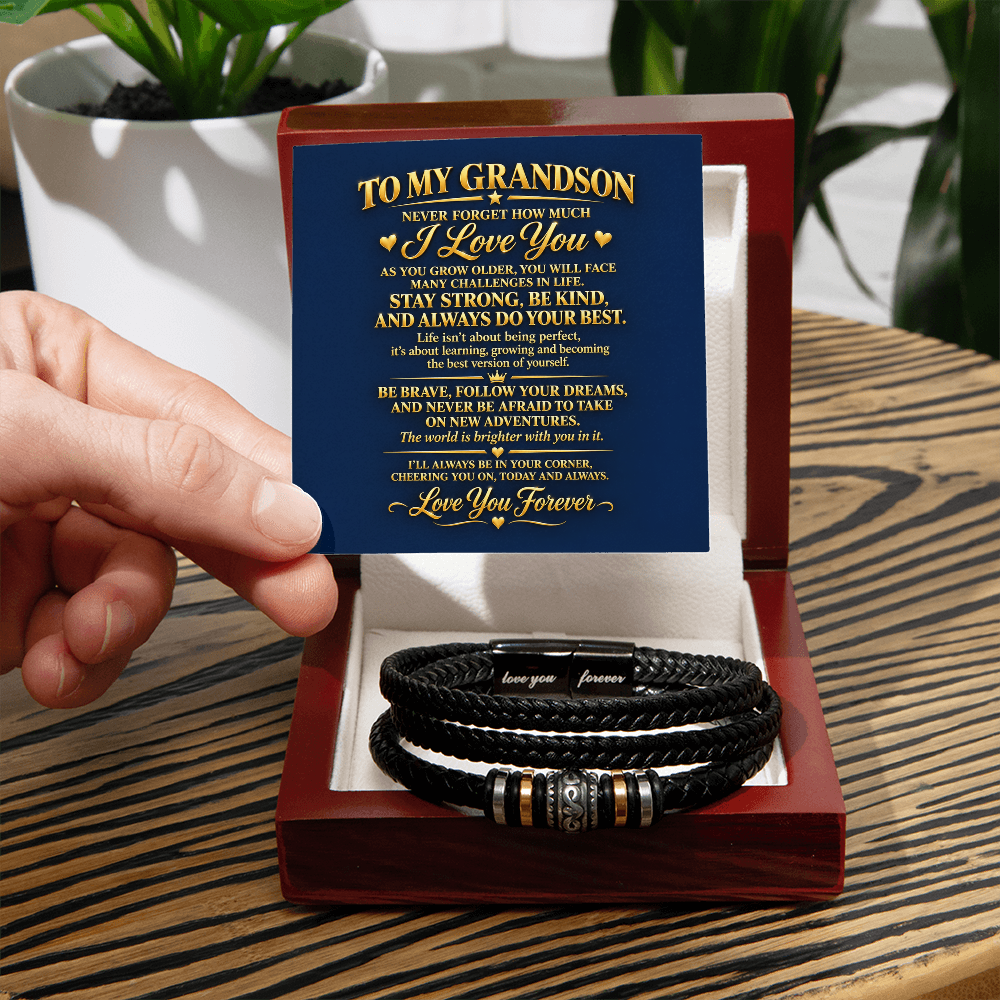 Grandson bracelet in an open mahogany-style gift box on a wooden table, with a hand holding the message card.