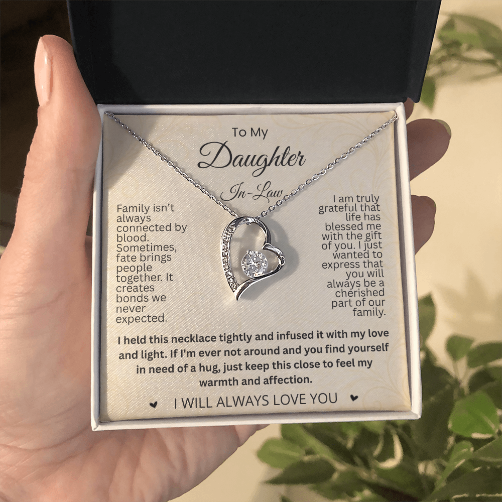 Hand holding a black and white gift box with a silver-tone heart necklace and cream daughter-in-law message card outdoors.
