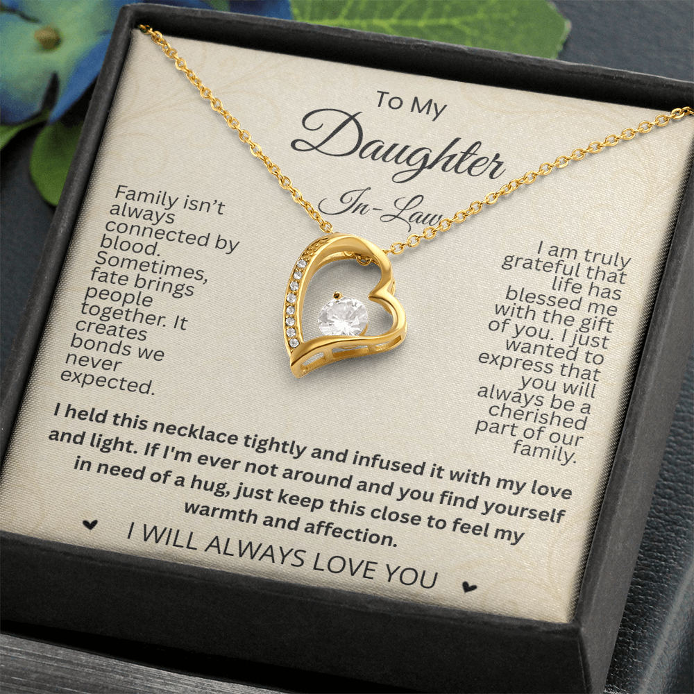 Close-up of a gold-tone heart necklace and daughter-in-law card in a black gift box beside greenery.